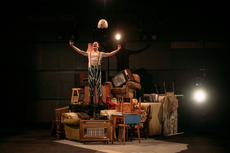 Actor standing on a large haphazard pile of furniture